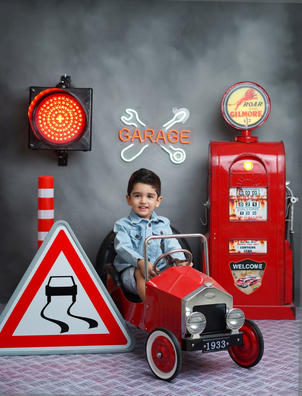 عکاسی کودک با دکور گاراژ قرمز در آتلیه تیرشات چیتگر، پسر بچه با لباس جین در ماشین کلاسیک قرمز